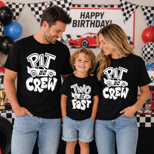 May include: Three black t-shirts featuring white graphic prints. Two shirts display the text "PIT CREW" with a race car graphic labeled "02". One shirt displays the text "TWO FAST" with a race car graphic labeled "02".