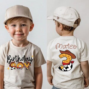 May include: A beige t-shirt with the words "Birthday Boy" in a playful font, featuring a cowboy hat and star accents. The back of the shirt has the name "Mateo" and a number 3 with a cowboy hat design. The child is wearing a beige baseball cap.