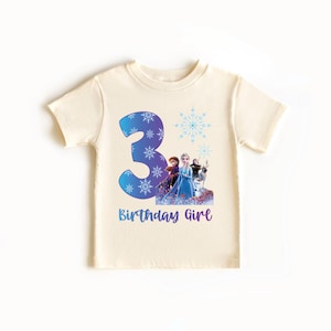 Pode incluir: Camiseta creme de manga curta com um grande n&uacute;mero 3 azul com detalhes de flocos de neve. Abaixo do n&uacute;mero, h&aacute; um gr&aacute;fico de personagens de um filme de anima&ccedil;&atilde;o popular e o texto "Birthday Girl".