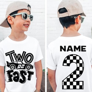 May include: A white t-shirt featuring a black graphic on the front with a race car and the text "TWO FAST". The back of the shirt displays the word "NAME" above a large number "2" with a black and white checkered pattern design.