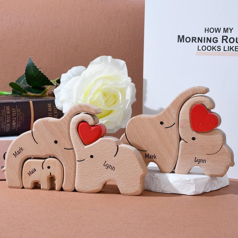 May include: Wooden elephant family figurines with red heart accents. Each elephant is engraved with a name. The text "HOW MY MORNING ROUTINE LOOKS LIKE" is visible in the background. The figurines are a light brown color.
