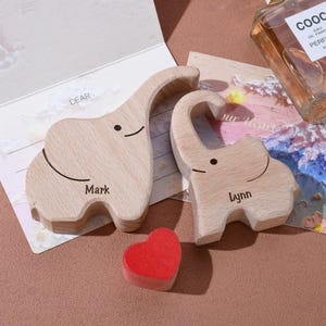 May include: Two wooden elephant figurines, one labeled "Mark" and the other "Lynn", with a small red heart. The elephants are light brown with black details. A greeting card with the word "DEAR" is visible.