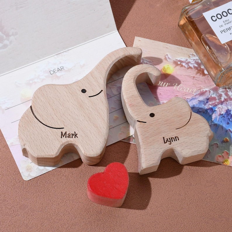 May include: Two wooden elephant figurines, one labeled "Mark" and the other "Lynn", with a small red heart. The elephants are light brown with black details. A greeting card with the word "DEAR" is visible.