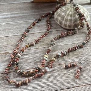 May include: A multi-strand necklace and matching earrings made with red, brown, and green jasper stone chips. The necklace is made with a silver chain.