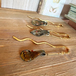May include: Four gold bookmark holders with glass accents. The glass accents are different colors and patterns. The bookmark holders are on a wooden surface.