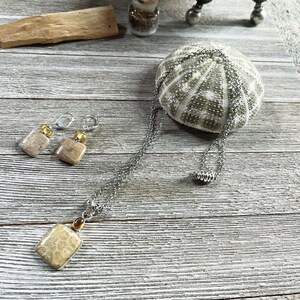 K&ouml;nnte beinhalten: Ein Set aus Ohrringen und einer Halskette mit versteinerten Korallen-Steinen in hellbrauner und beigefarbener Farbe. Die Steine sind quadratisch und haben eine nat&uuml;rliche, organische Textur. Der Schmuck ist aus einer silbernen Kette und gelben Perlen gefertigt.