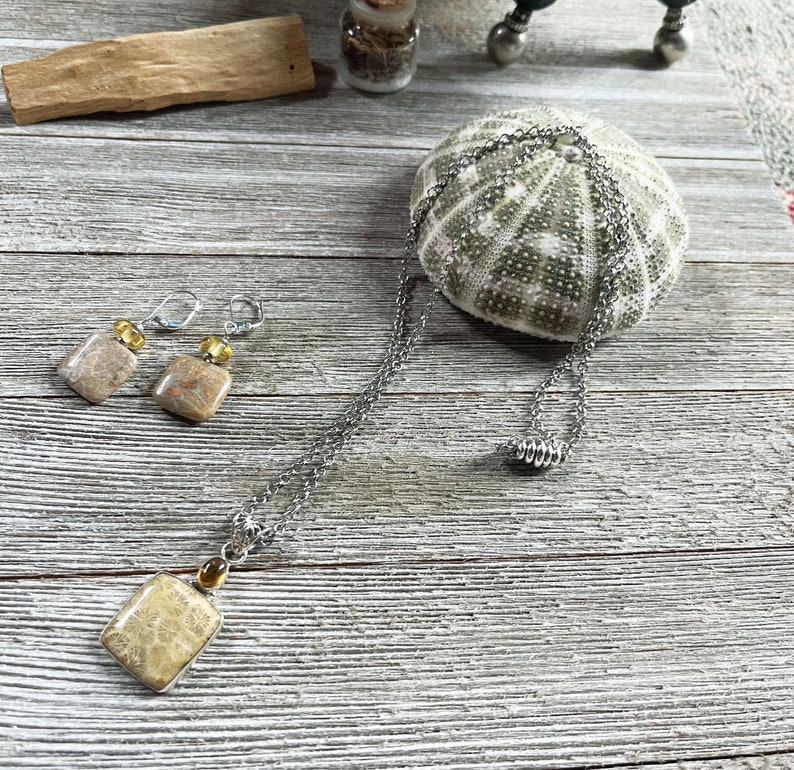 K&ouml;nnte beinhalten: Ein Set aus Ohrringen und einer Halskette mit versteinerten Korallen-Steinen in hellbrauner und beigefarbener Farbe. Die Steine sind quadratisch und haben eine nat&uuml;rliche, organische Textur. Der Schmuck ist aus einer silbernen Kette und gelben Perlen gefertigt.