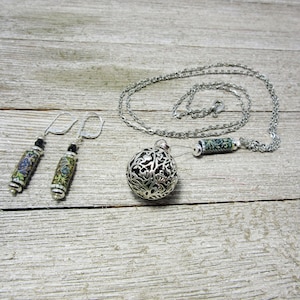 Könnte beinhalten: Eine silberne Halskette mit einem silbernen Anhänger in Form eines Baumes mit floralem Design. Die Halskette hat eine silberne Kette und ein silbernes Röhrchen mit floralem Design. Die Halskette wird mit einem Paar silberner Ohrringe mit floralen Designs geliefert.