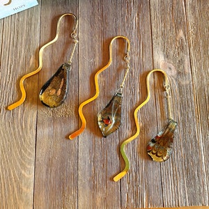 May include: Four gold bookmark holders with decorative glass accents. Each bookmark features a different design with shades of brown, gold, and red.