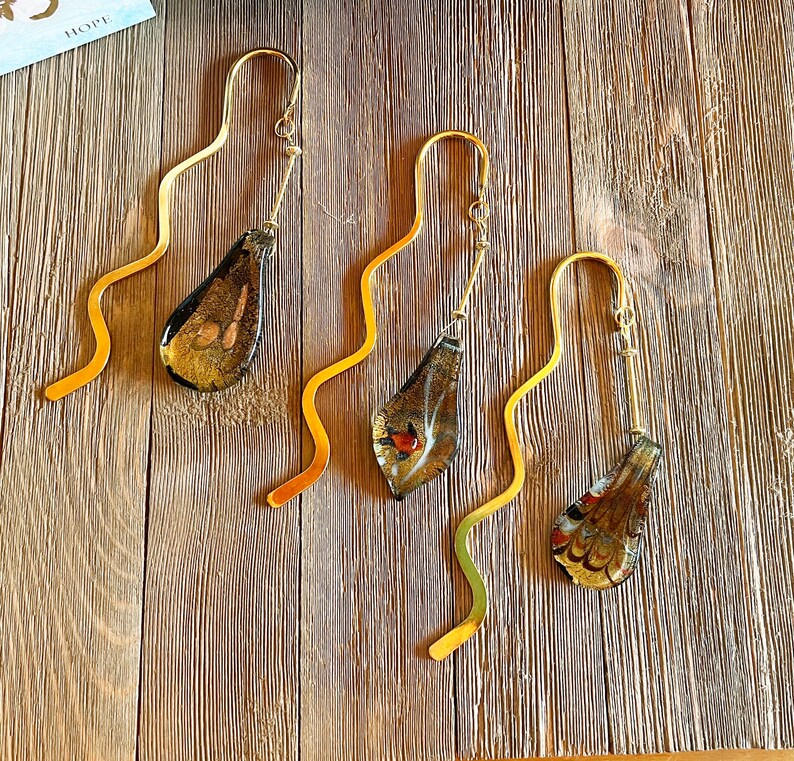 May include: Four gold bookmark holders with decorative glass accents. Each bookmark features a different design with shades of brown, gold, and red.