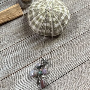 May include: A silver chain necklace with a multi-colored stone pendant. The pendant features a variety of stones, including pink, green, and brown. The necklace is displayed on a wooden surface.