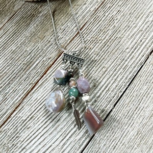 May include: A silver chain necklace with a multi-colored stone pendant. The pendant features a variety of stones, including pink, green, and brown. The stones are arranged in a cluster and are attached to a silver chain.