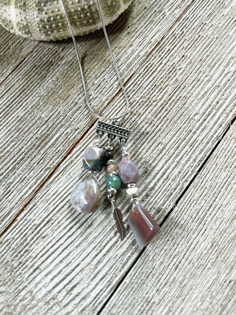 May include: A silver chain necklace with a multi-colored stone pendant. The pendant features a variety of stones, including pink, green, and brown. The stones are arranged in a cluster and are attached to a silver chain.