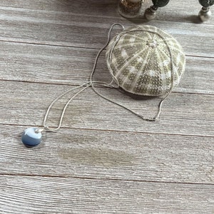 May include: A silver chain necklace with a round, gray and white agate pendant. The necklace is lying on a wooden surface.