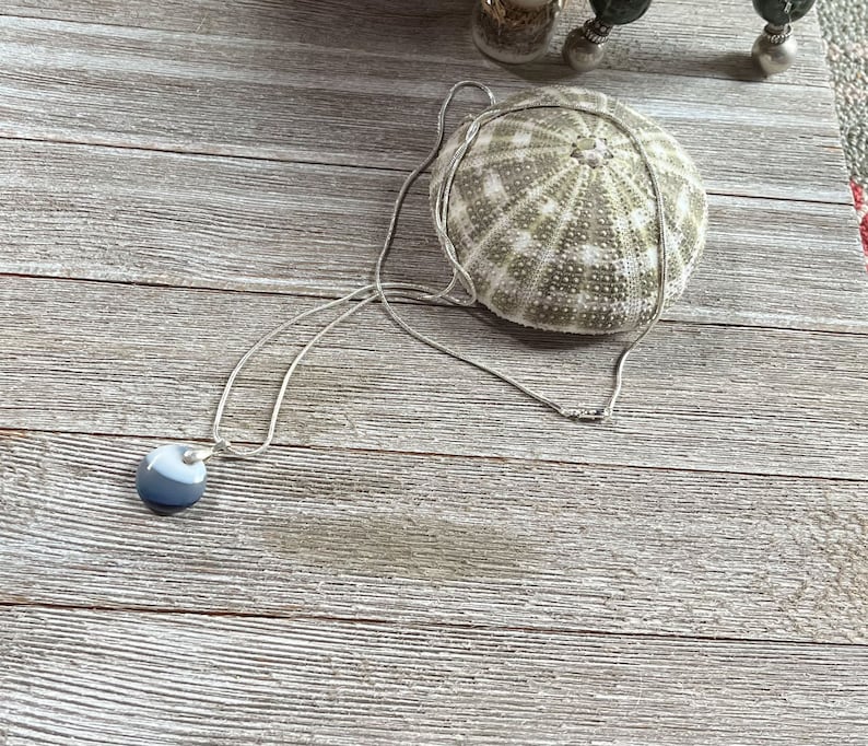 May include: A silver chain necklace with a round, gray and white agate pendant. The necklace is lying on a wooden surface.