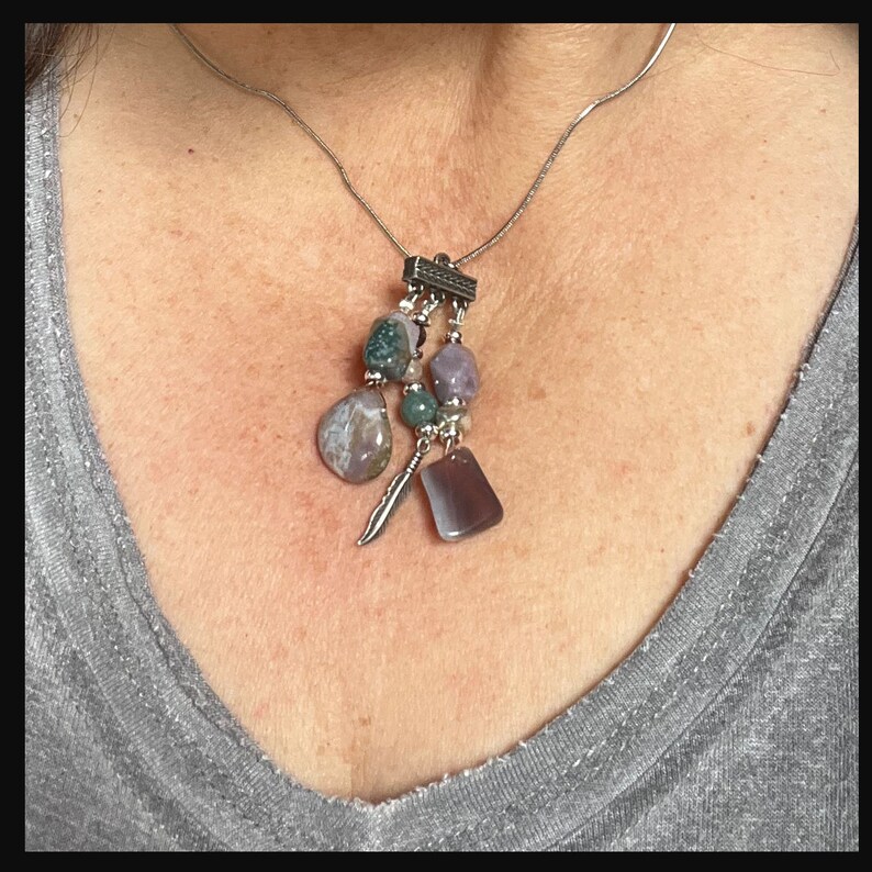 May include: A silver chain necklace with a silver pendant featuring a cluster of purple, green, and white stones. The pendant is attached to the chain with a silver bar.