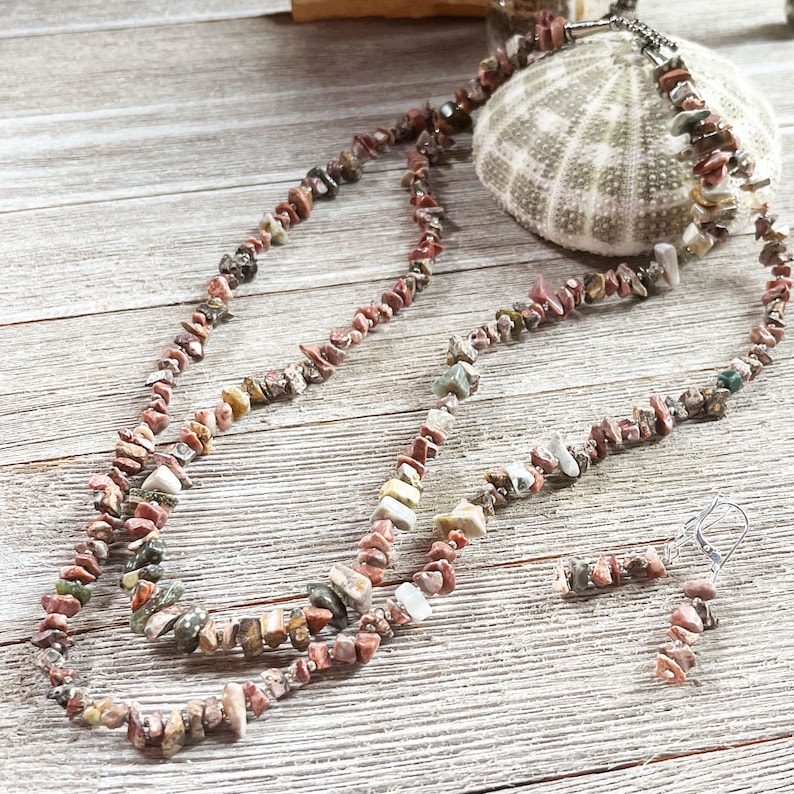 May include: A multi-strand necklace and matching earrings made of small, irregular, multi-colored stones. The stones are a mix of pink, brown, green, and white.