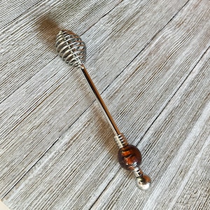 May include: A silver honey dipper with a coiled metal head and a brown glass handle.