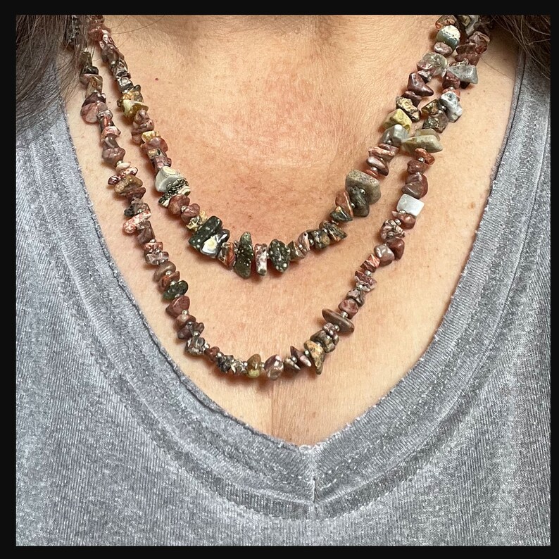 May include: Two layered necklaces made of small, irregularly shaped, multi-colored stones. The stones are a mix of brown, red, green, and white.