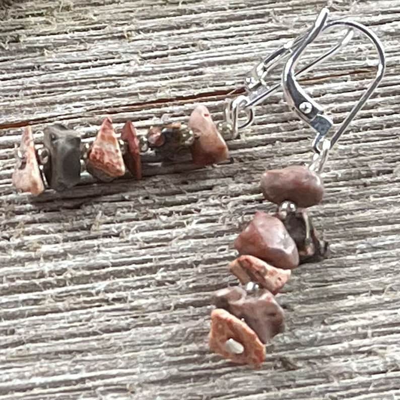 May include: A pair of earrings with a silver hook and a chain of red, brown, and black stones.