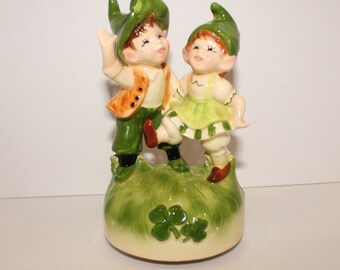 Seated Baby Green Elf Pixie Leprechaun Figurine Holding Shamrocks Clovers Peapod Green Suit Flower Hat Brown Hair Japan 1970s