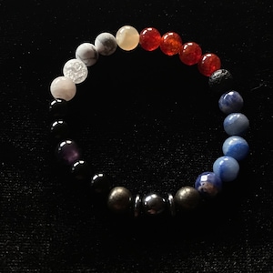 May include: A beaded bracelet featuring a range of colours and textures, including white, grey, yellow, orange, red, black, blue, and brown.