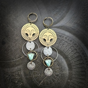 Może przedstawiać: Para długich, zwisających kolczyków o tematyce niebiańskiej. Każdy kolczyk ma mosiężny dysk słoneczny, srebrne kółka, turkusowy klejnot i małą srebrną monetę. Kolczyki mają styl vintage i boho.