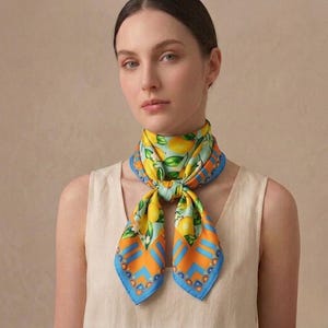 Peut inclure: Un foulard en soie avec un motif de citrons jaunes, verts et bleus. Le foulard carré est noué autour du cou. La bordure présente un motif géométrique orange et bleu. Un accessoire élégant.