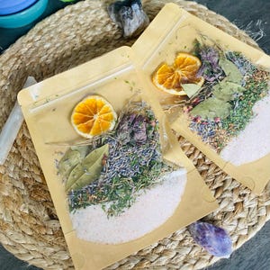 May include: Two brown paper bags with zipper closures filled with dried herbs, flowers, and orange slices. The bags are on a woven straw surface.