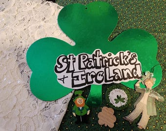 May include: A collection of St. Patrick's Day decorations, including a large green shamrock with the text "St. Patrick's Ireland", a leprechaun figure, and other festive ornaments. The items are set against a green patterned background.