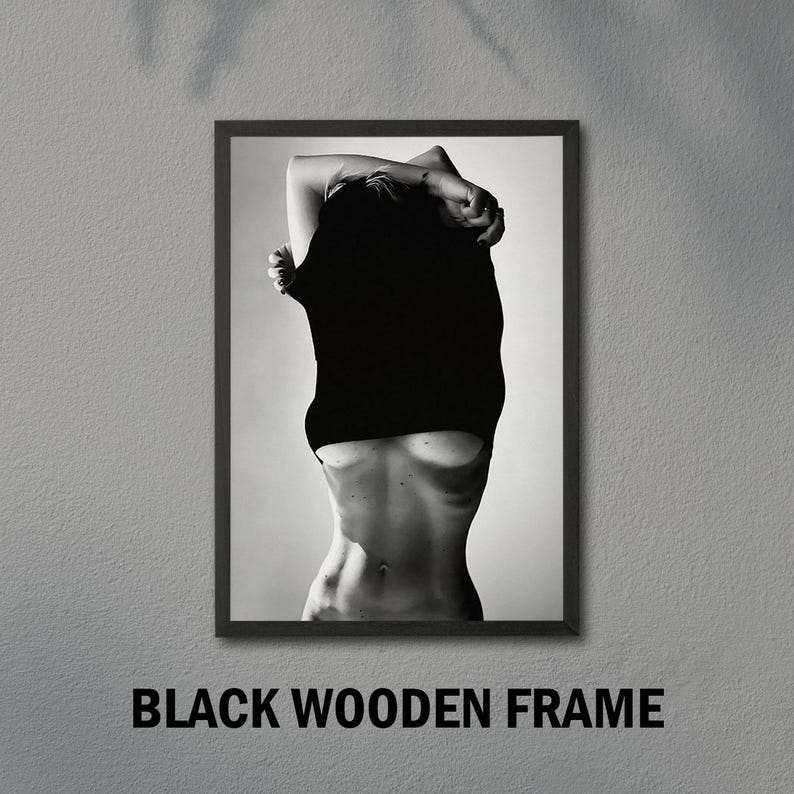 May include: Black and white photo of a person pulling a black shirt off their shoulders, revealing their torso.