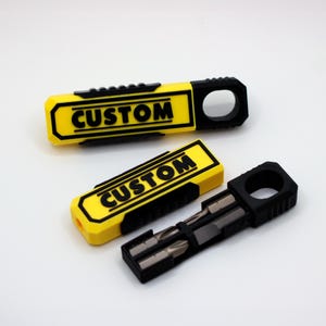 May include: Two yellow and black multi-tool keychains with the word "CUSTOM" in black. One keychain is open, revealing several small metal bits. The keychains have a black ring on one end.