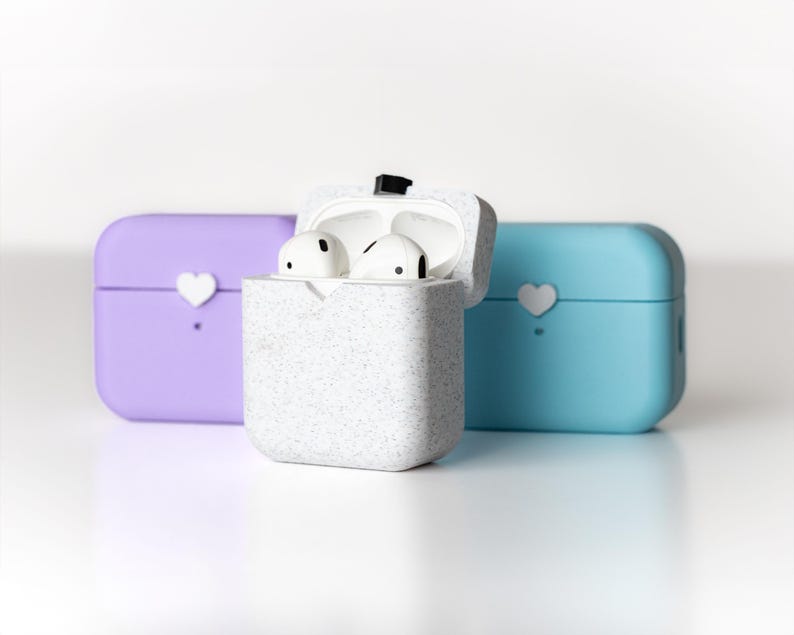 Pu&ograve; includere: Tre custodie per AirPod, una blu chiaro, una viola e una bianca con un motivo maculato. La custodia bianca &egrave; aperta, rivelando due auricolari AirPod bianchi.
