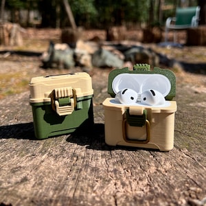 May include: Two green and beige protective cases for wireless earbuds. One case is open and shows two white earbuds inside. The cases have a latch and a handle.