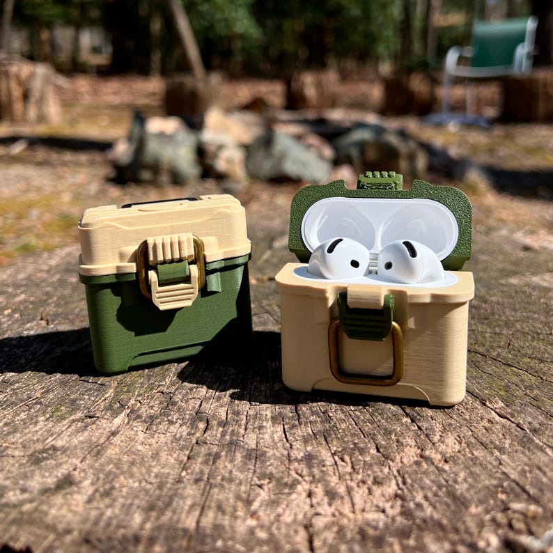 May include: Two green and beige protective cases for wireless earbuds. One case is open and shows two white earbuds inside. The cases have a latch and a handle.