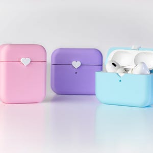 Pu&ograve; includere: Tre custodie in silicone per auricolari wireless. Le custodie sono rosa, viola e blu chiaro. La custodia blu chiaro &egrave; aperta e mostra due auricolari bianchi all'interno.