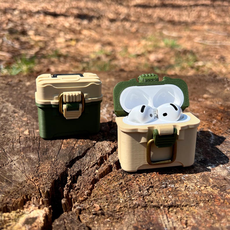 May include: Two small, beige and green, plastic cases with a latch closure. One case is open and shows white wireless earbuds inside. The cases resemble miniature toolboxes.