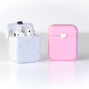 Pu&ograve; includere: Due custodie per auricolari wireless, una bianca con una texture punteggiata e l'altra rosa con un cuore bianco sul davanti.