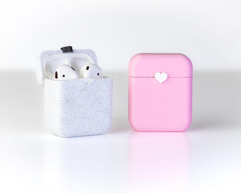 Pu&ograve; includere: Due custodie per auricolari wireless, una bianca con una texture punteggiata e l'altra rosa con un cuore bianco sul davanti.