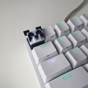 Puede incluir: Un teclado mecánico blanco con una tecla panda en blanco y negro. El teclado tiene retroiluminación verde en las teclas "tab", "caps" y "shift".