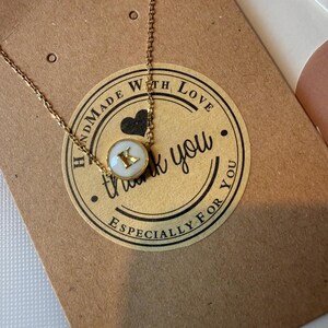 May include: A gold necklace with a pendant displaying the letter "K" on a white background. The necklace rests on a brown card with a sticker that reads "Handmade with Love", "thank you", and "Especially for you".