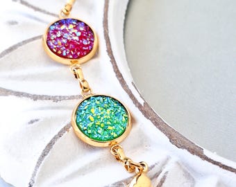 May include: A gold-toned bracelet with three circular, sparkling gemstone charms. The charms are white, red-purple, and green-yellow, each set in a gold bezel. The bracelet has a lobster clasp closure.