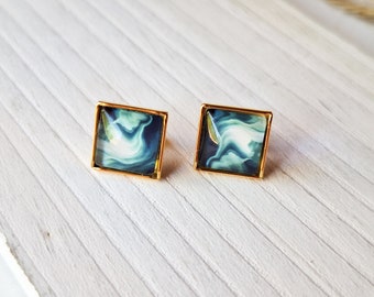 May include: A pair of square-shaped earrings with a gold frame and a blue and white marbled design.