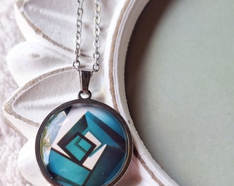 May include: A silver chain necklace with a round pendant featuring a geometric design in shades of blue, white, and black.