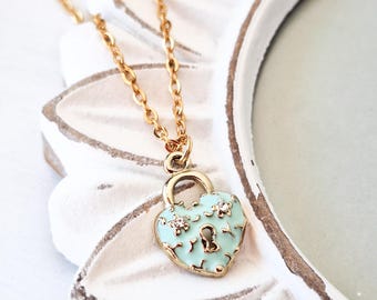 May include: A gold chain necklace with a heart-shaped padlock pendant. The padlock is light blue with gold accents and has a keyhole and small rhinestones.
