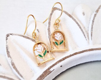 May include: Gold tone earrings with a white flower and green leaves inside a gold cage design.
