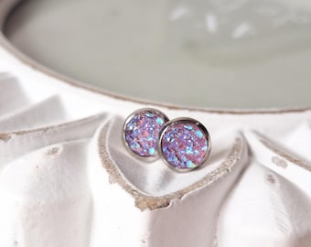 May include: A pair of silver stud earrings with iridescent purple and pink glitter embedded in the round face.