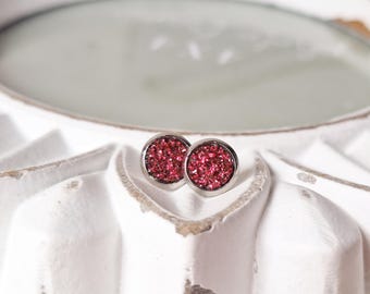 May include: A pair of silver stud earrings with pink glitter accents.