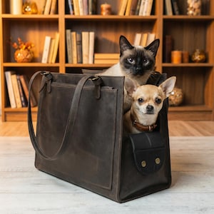 May include: A brown leather tote bag with a Siamese cat and a Chihuahua inside. The tote has a front pocket and handles. The cat has blue eyes and a dark face. The dog wears a brown collar.