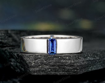 May include: A silver band with a rectangular blue sapphire gemstone set in the center.